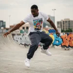 Jeune danseur urbain pratiquant le krump dans une place en béton couverte de graffitis colorés en 2026
